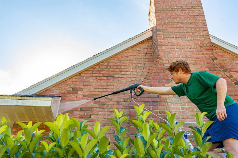 man washing the roof of a brick house