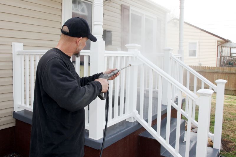 a man with a cap pressure washing the entrance stairs