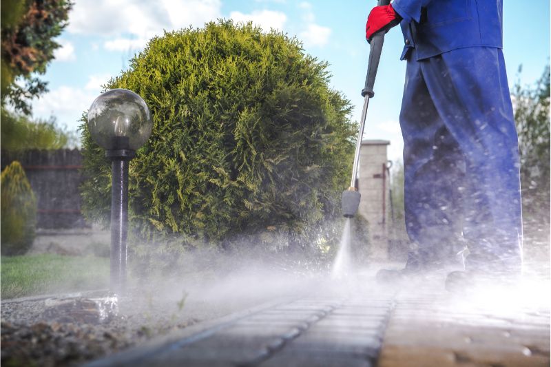 a person in blue suit pressure washing the driveway