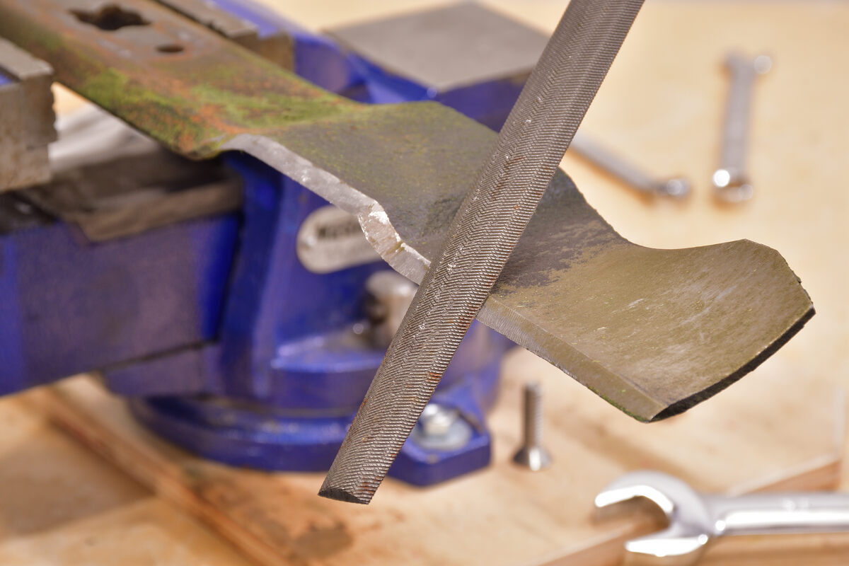 person sharpening lawnmover blade with a file