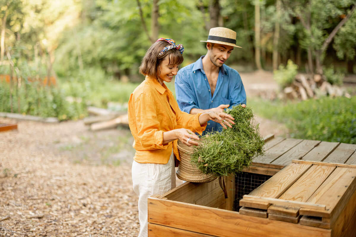 Young couple throwing cut grass into wooden compost bin