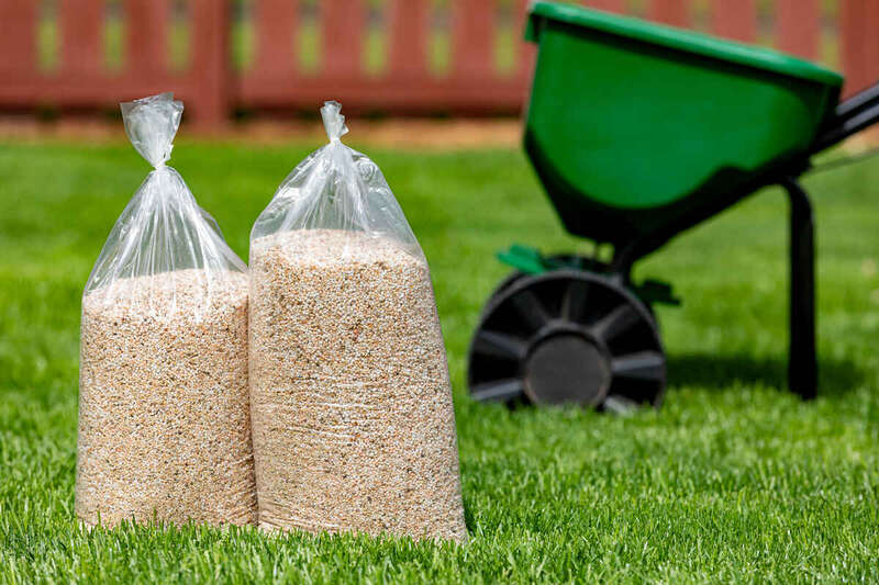 bags of lawn fertilizer and herbicide sitting on a lawn with a fertilizer spreader in the backyard