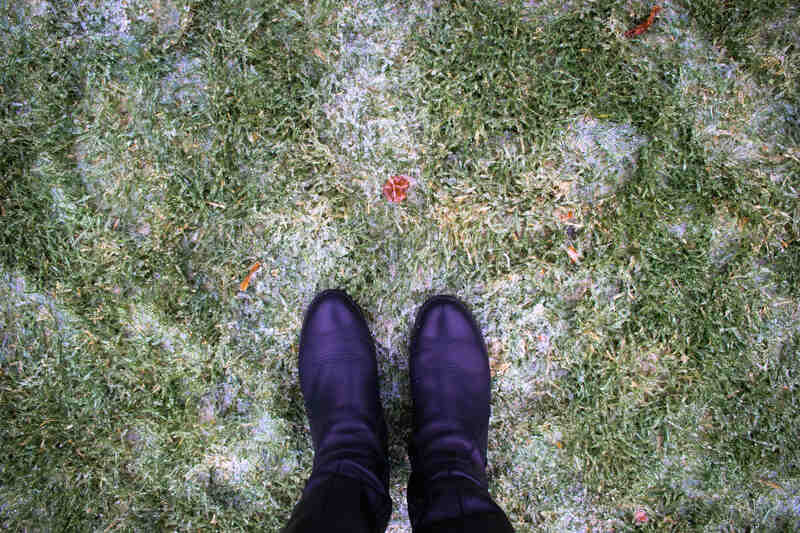 Legs in boots against the background of frozen lawn covered with ice with green grass.