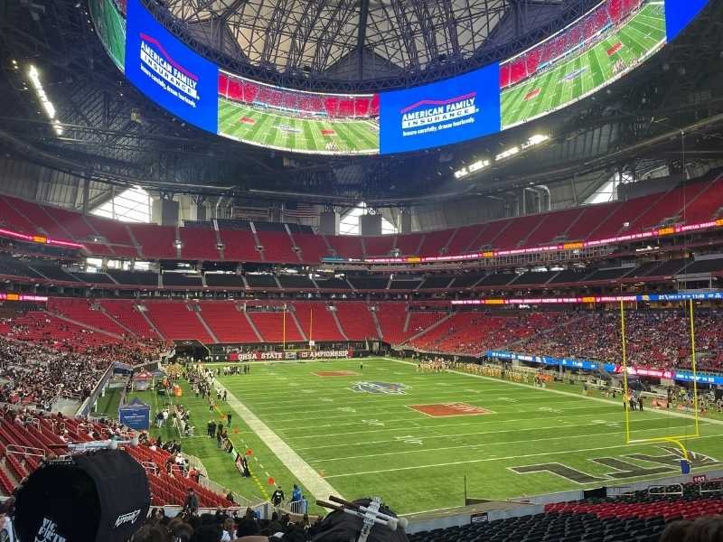 Interior of Mercedes-Benz Stadium during football game, featuring massive circular video board.