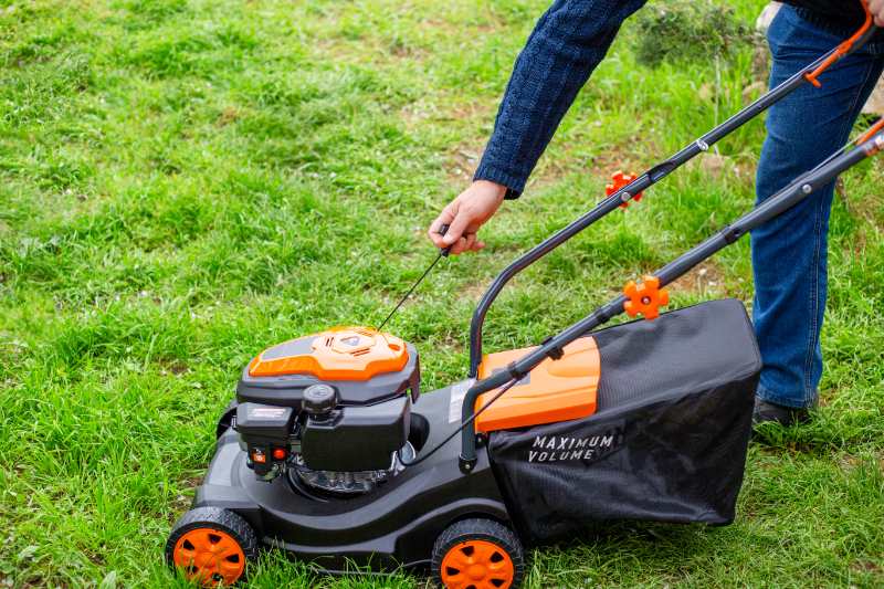 A man starts the engine of a gas lawn mower with a starter rope